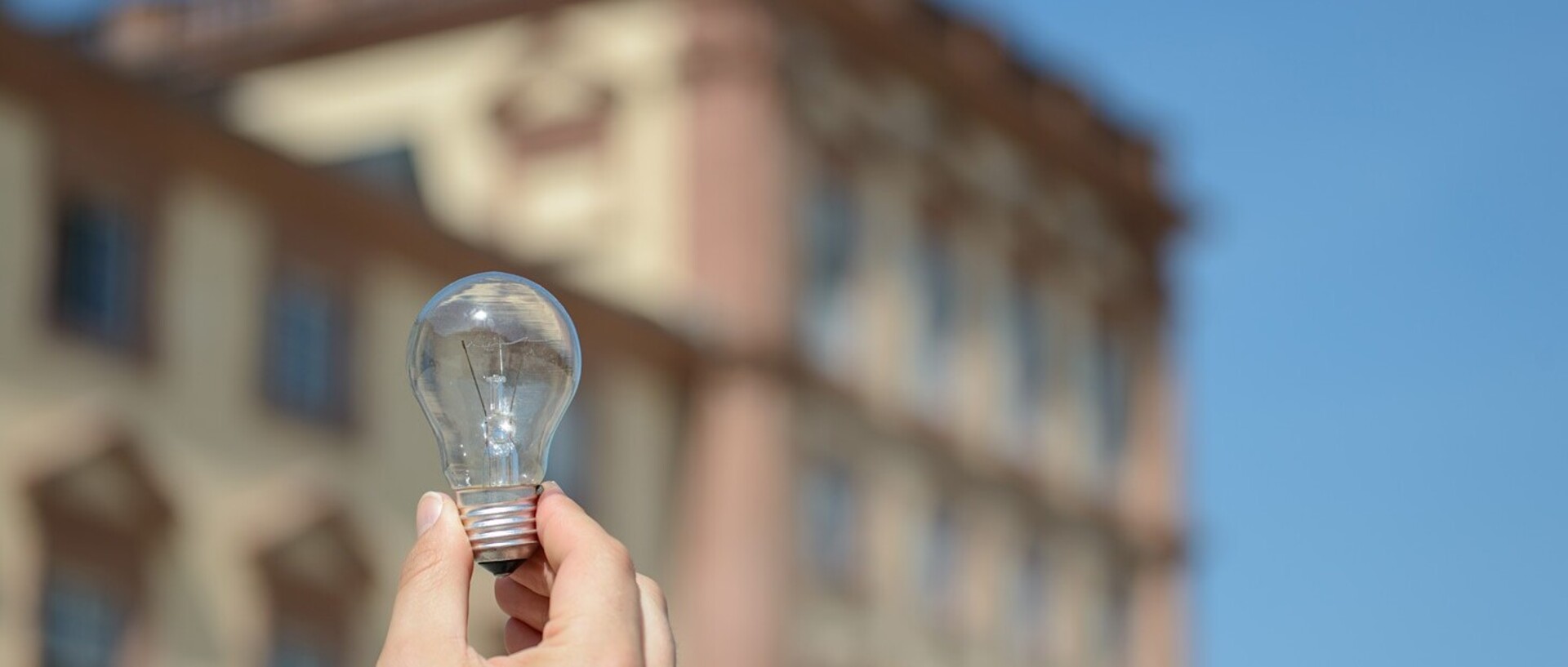Eine Hand hält eine Glühlampe. Im Hintergrund befinden sich Teile des Mannheimer Barockschlosses.