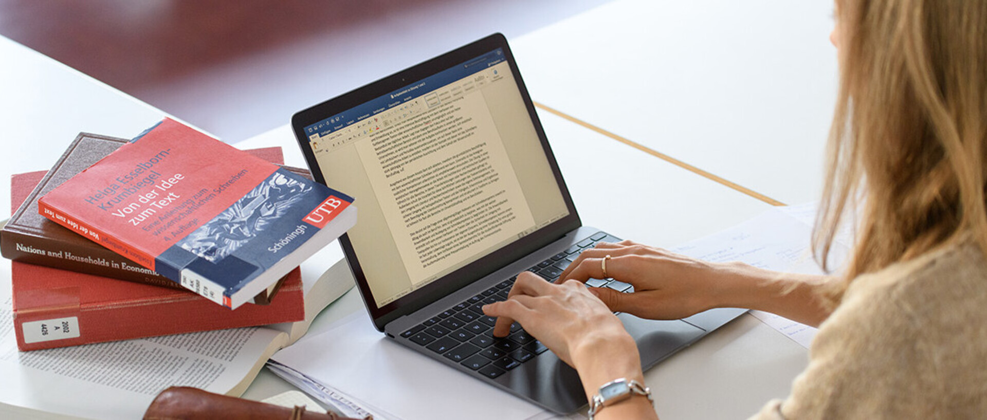 Student at her laptop with books on scientific working.