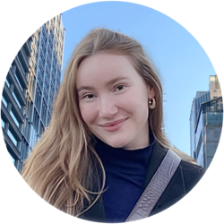 Portrait von Henriette, einer Bachelorstudentin der Volkswirtschaftslehre. Sie hat rötliche lange Haare und trägt ein dunkelblaues Oberteil und darüber eine schwarze Jacke. Sie steht vor Gebäuden von Seoul.