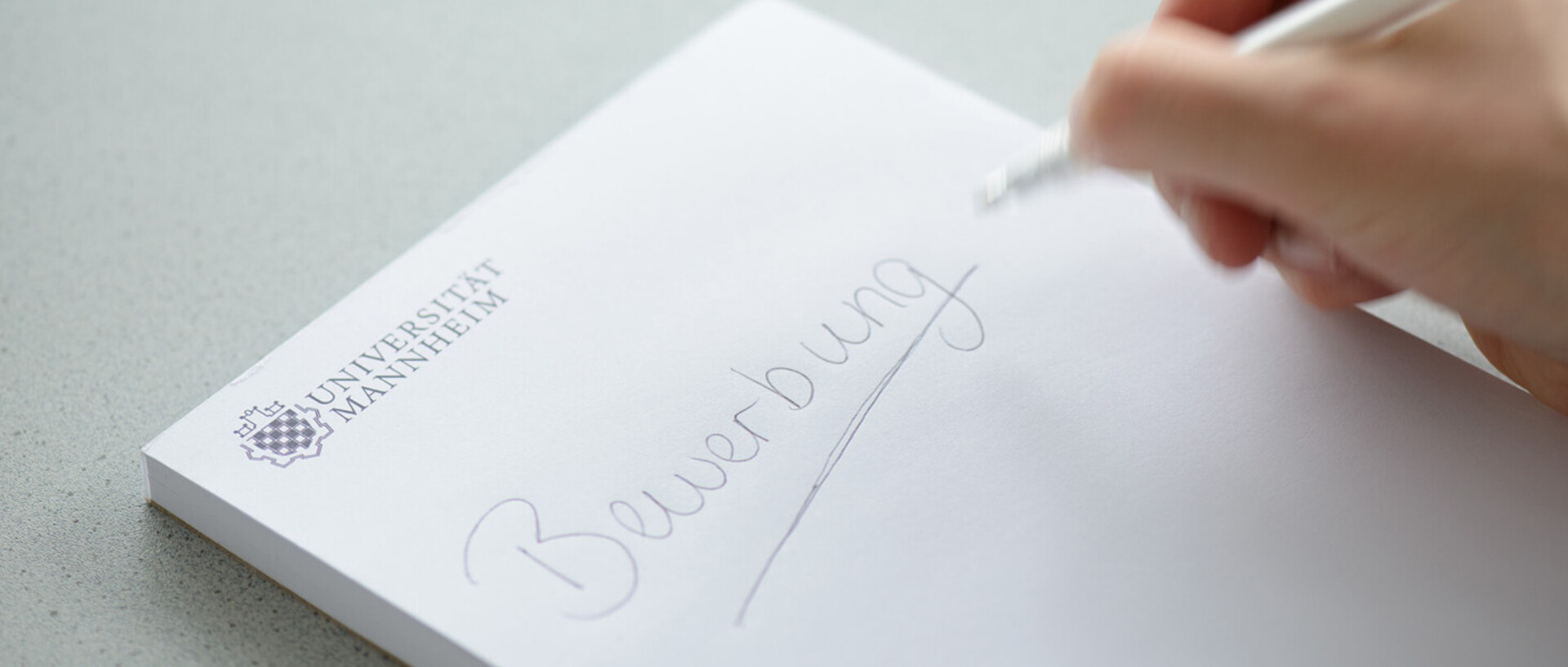 On a blank white pad with the logo of the University of Mannheim in the top left-hand corner, ‘Bewerbung’[Application] is written and underlined with a biro in black.