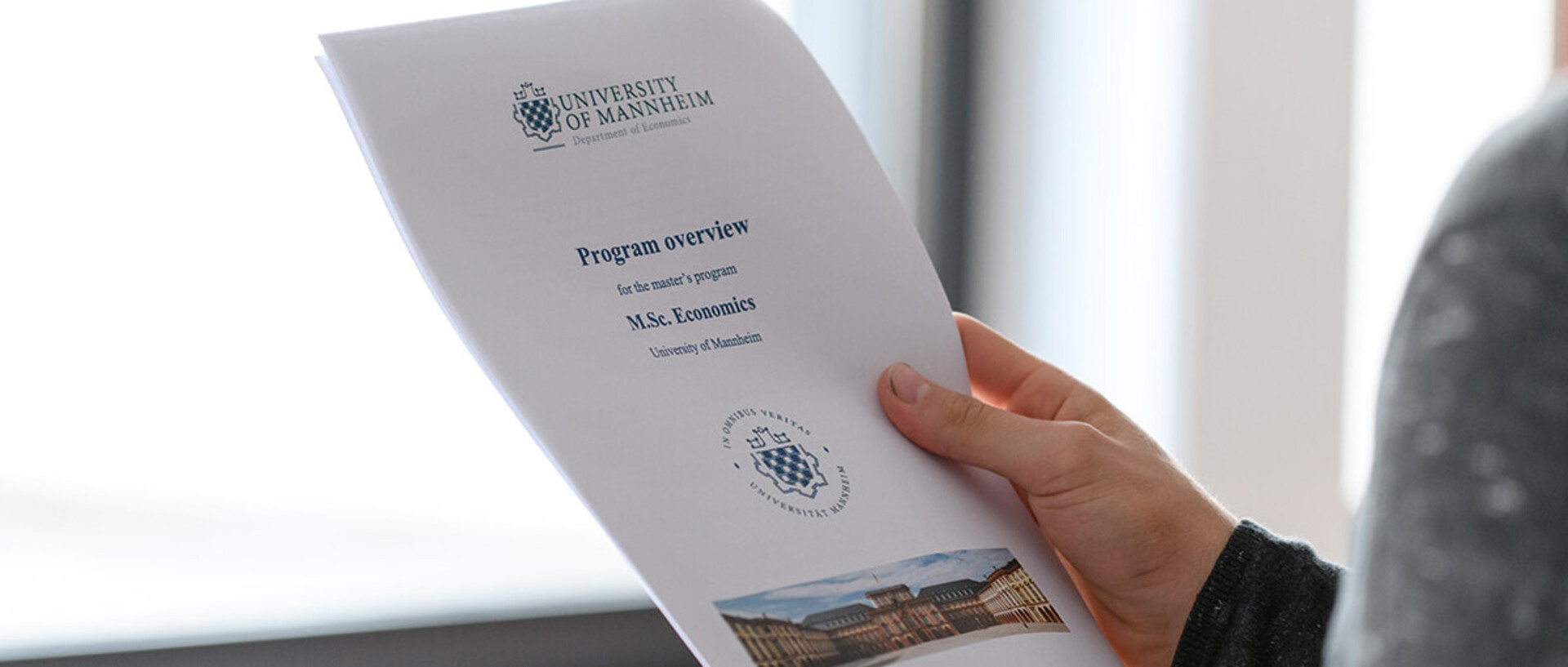 One person holds a printout of the overview of the master’s program in their hands.