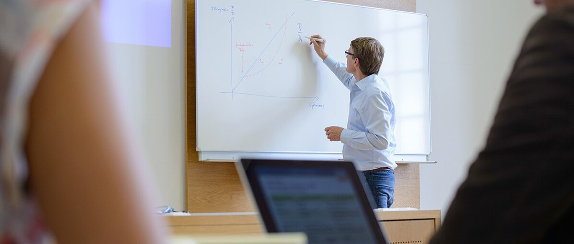 Professor Adam writes on a whiteboard in a lecture theatre.
