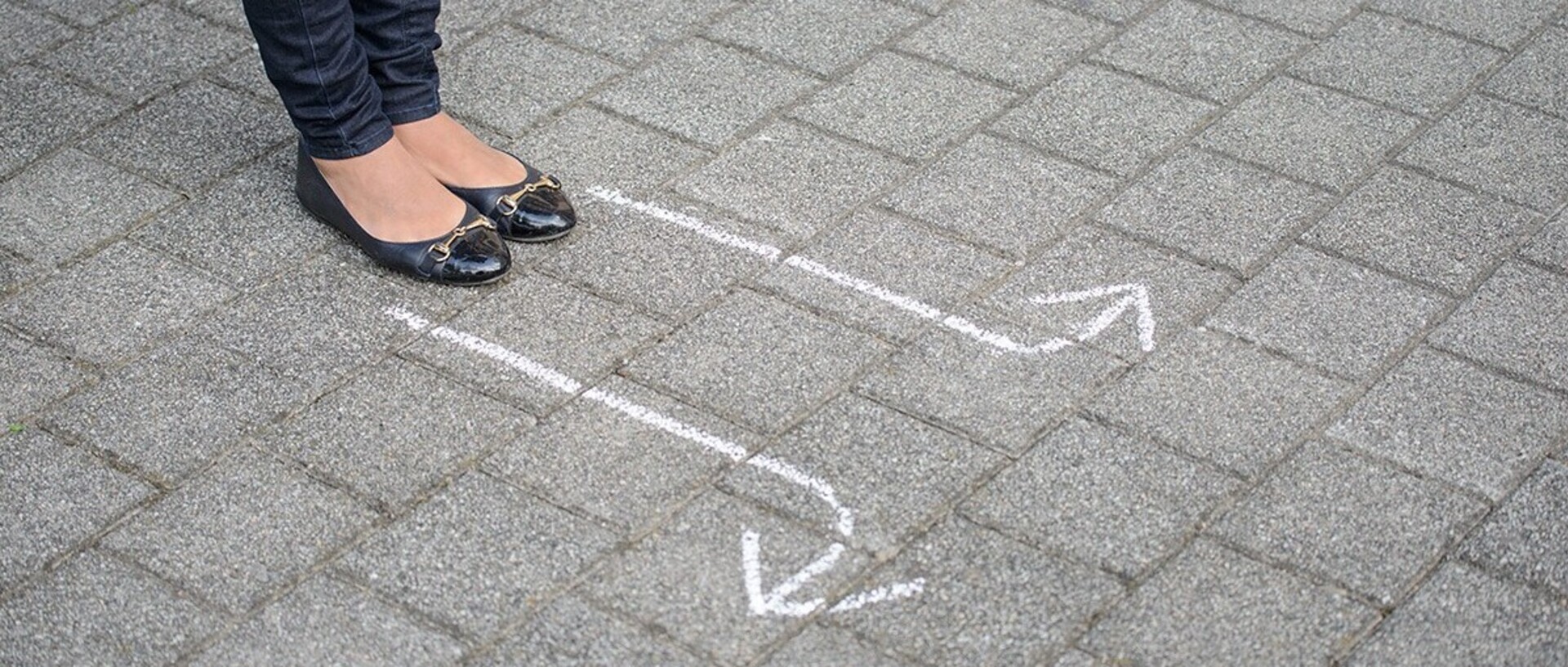 Frau in dunkler Hose steht vor zwei Pfeilen auf dem Boden, die in entgegengesetzte Richtungen zeigen.