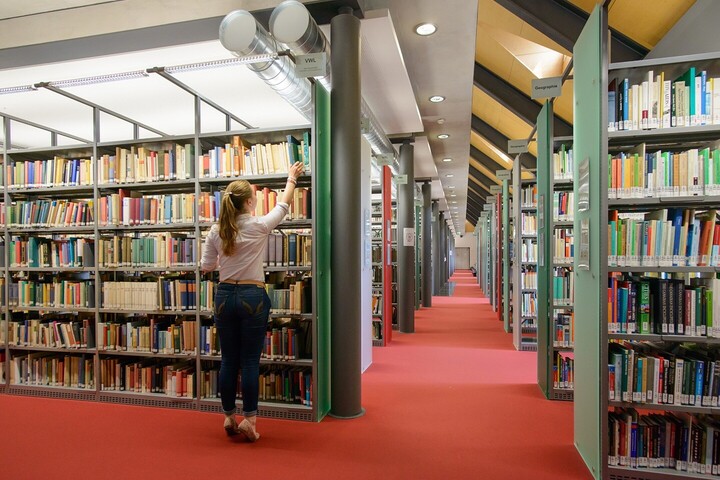 View of the “Ehrenhof“-Library. A student takes a book from one of the shelves.