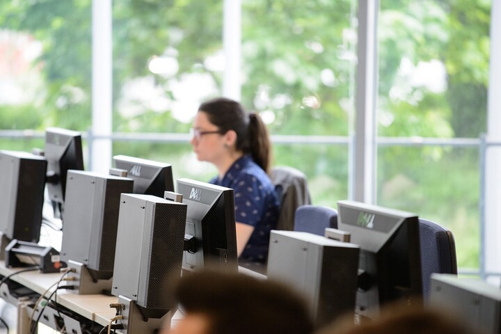 Blick in den VWL PC-Pool. Am Ende einer Reihe von Bildschirmen sitzt eine Studentin mit braunen Haaren und blauem Shirt vor einem der Bildschirme. 
