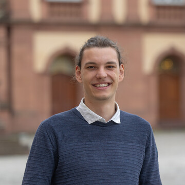 Konrad Strehl. Er trägt einen dunklen Pullover über einem weißen Hemd und steht auf dem Ehrenhof des Mannheimer Schlosses.