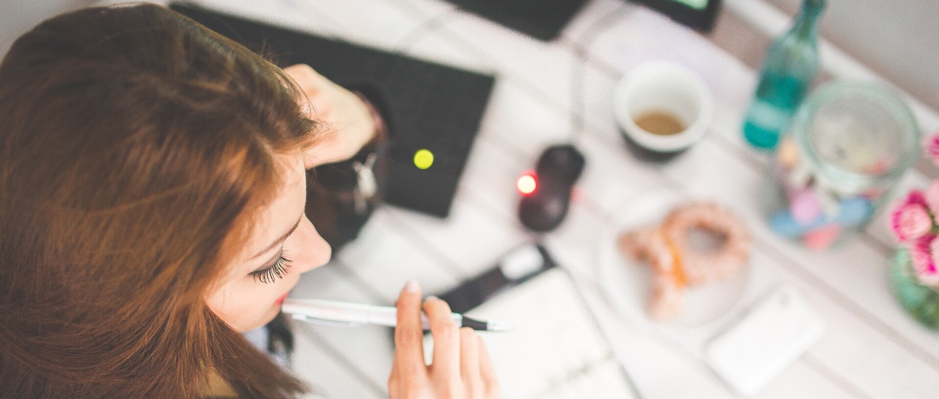 A brown-haired woman looks at a calendar in front of her. She is holding a white biro in her hand.