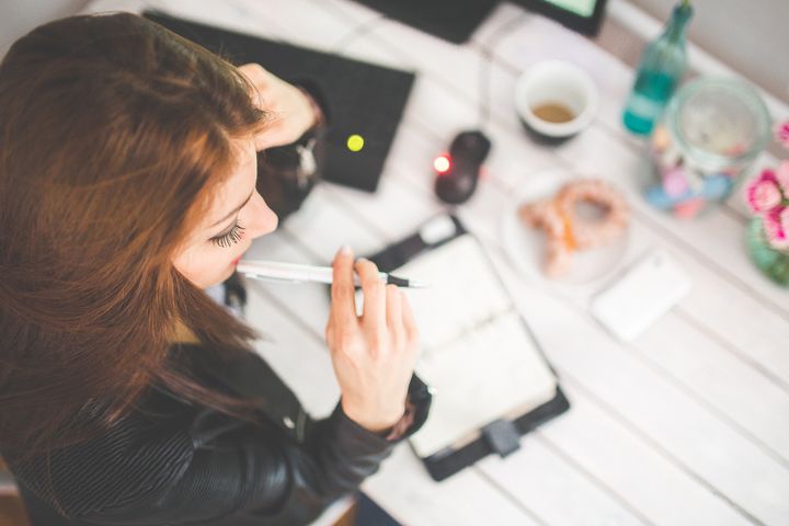 A brown-haired woman looks at a calendar in front of her. She is holding a white biro in her hand.