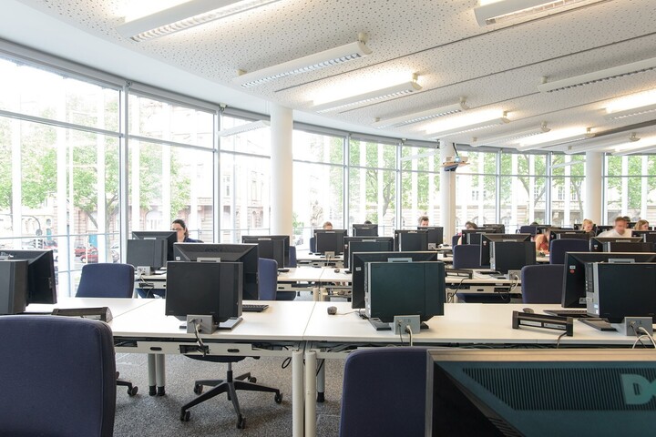 Blick von Vorne in den PC-Pool der Abteilung VWL. An einigen PCs sitzen Studierende.