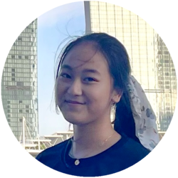 Portrait von Ha My, einer Bachelorstudentin der Volkswirtschaftslehre. Sie hat die langen schwarzen Haare zu einem Zopf gebunden und trägt ein dunkles Oberteil und dazu eine goldene Kette. Sie steht vor Gebäuden von Singapur.