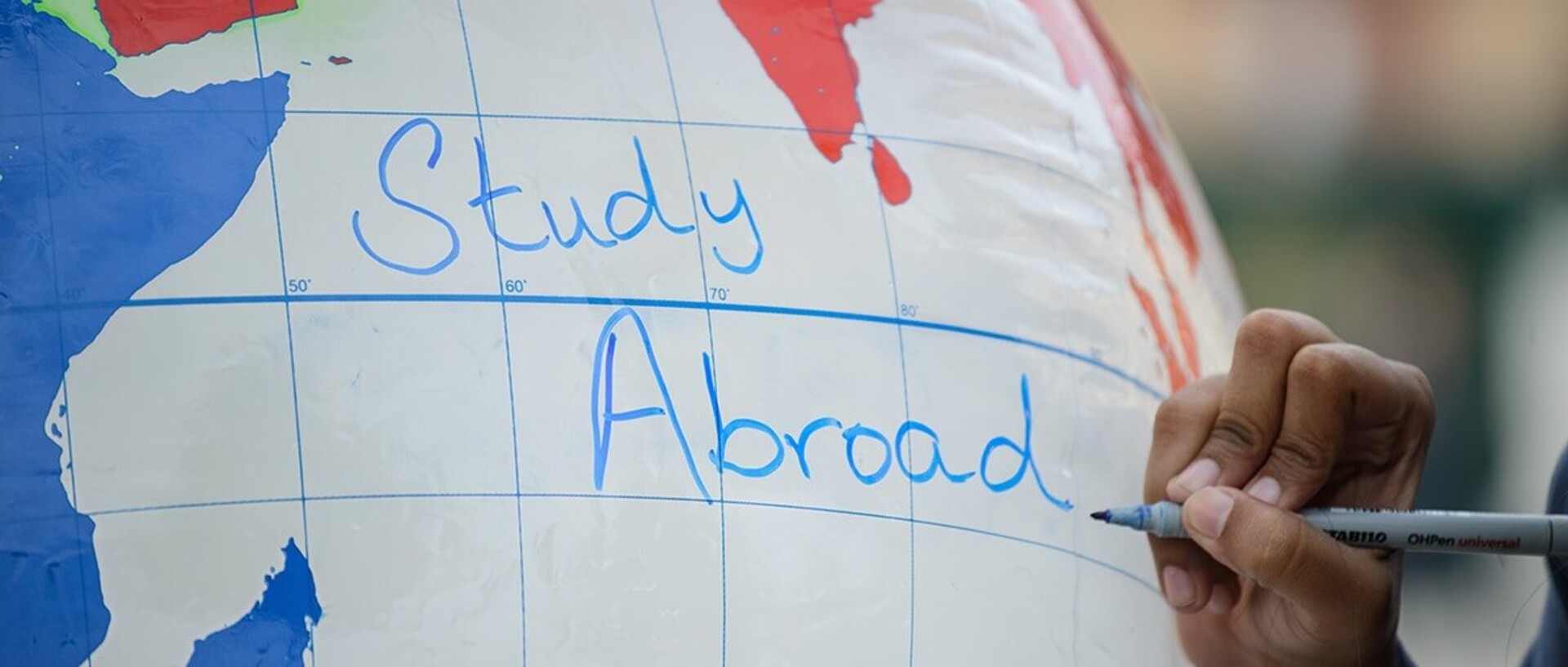 Mit einem blauen Stift wird auf eine große Weltkugel „Study Abroad“ geschrieben.
