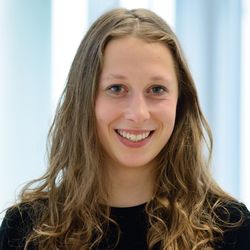Portrait von Naemi, einer Studentin der Volkswirtschaftslehre. Sie hat mittellange blonde wellige Haare und trägt ein schwarzes Oberteil. Naemi lächelt in die Kamera. 