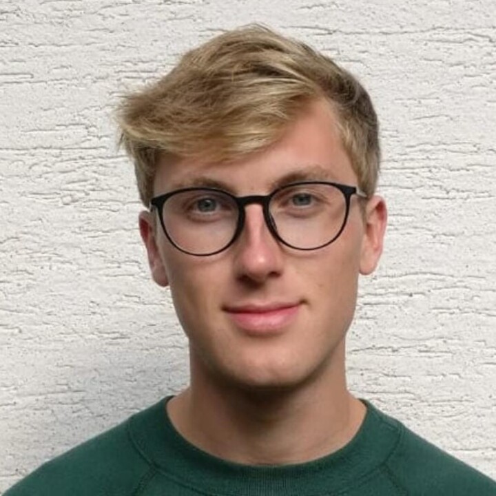 Florian Frühhaber hat kurze blonde Haare. Er trägt eine runde Brille und ein dunkelgrünes Oberteil.