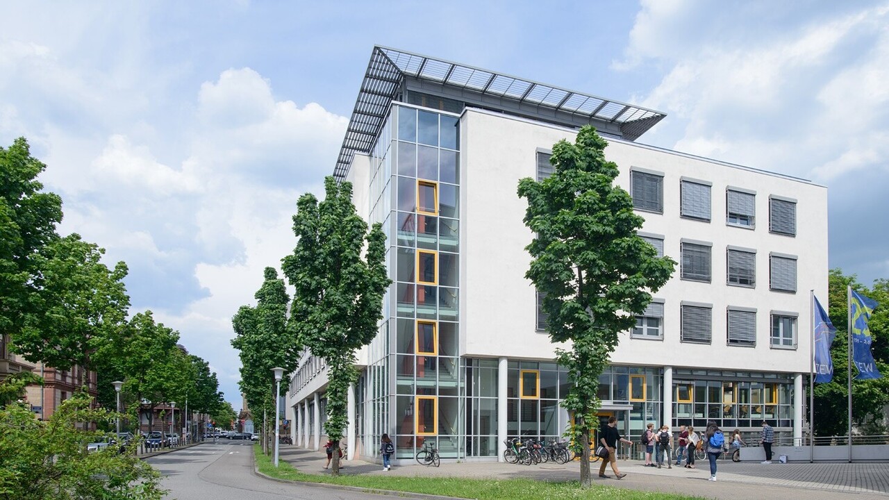 Blick auf die Rückseite des Gebäudes der Abteilung Volkswirtschaftslehre. Im Vordergrund befinden sich eine Straße und einige Bäume.