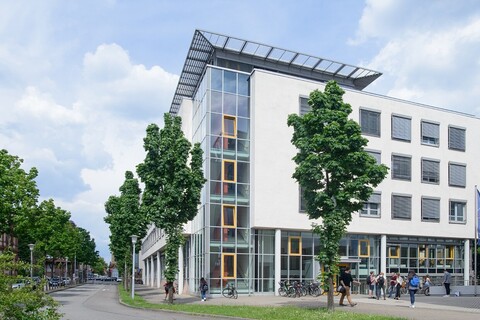 Blick auf die Rückseite des Gebäudes der Abteilung Volkswirtschaftslehre. Im Vordergrund befinden sich eine Straße und einige Bäume.