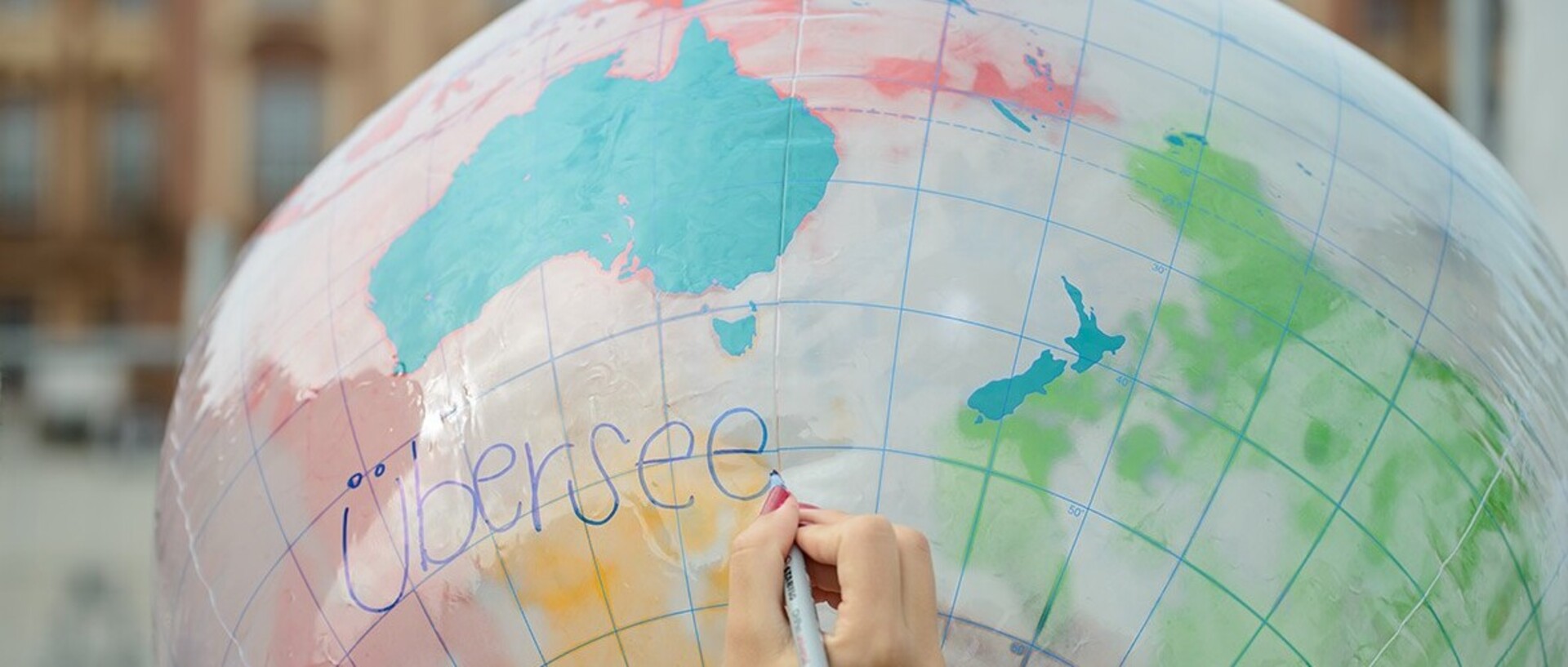 Auf einen aufgeblasenen Globus wird „Übersee“ mit einem blauen Stift geschrieben.