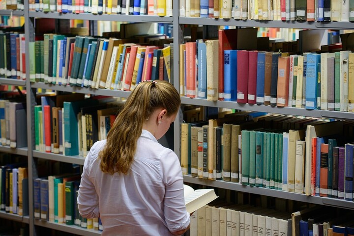 Eine Studentin mit einem Buch an einem der Regale der VWL-Bibliothek.