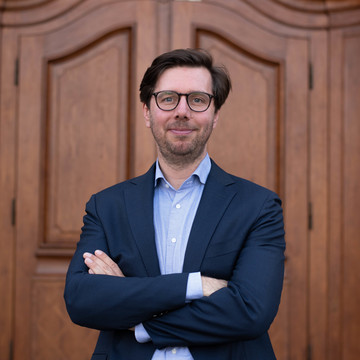 Prof. Dörrenberg hat braunes Haar, trägt eine Brille, ein hellblaues Hemd und einen dunkelblauen Anzug.