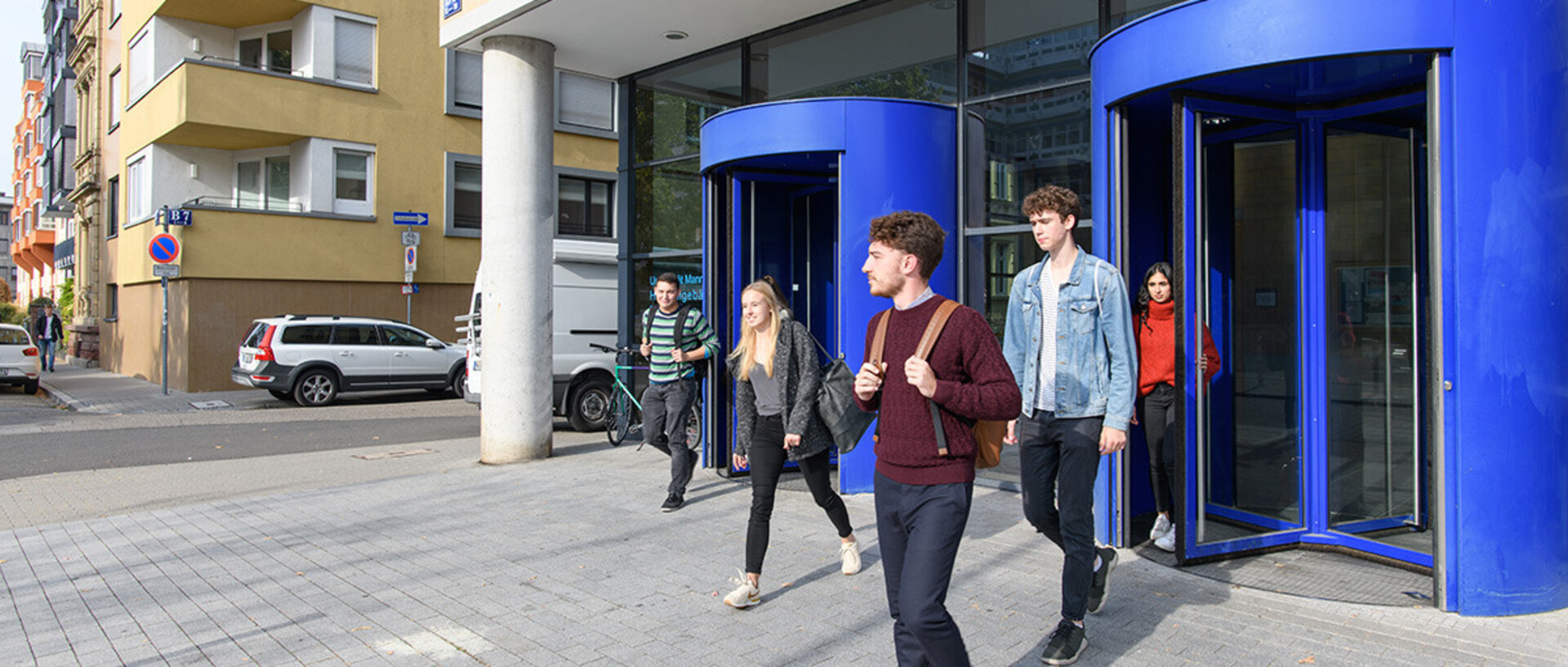 Einige Studierende verlassen das Gebäude B6 durch die dunkelblau eingefassten Drehtüren.