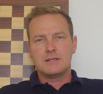 Hans Peter Grüner hat kurze graue Haare. Er trägt ein dunkles Oberteil und blickt in die Kamera.