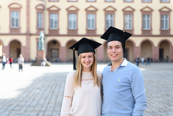 Eine Bachelorabsolventin und ein Bachelorabsolvent stehen vor dem Mannheimer Schloss.