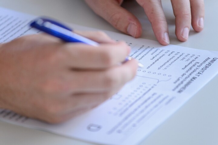 Eine Person füllt mit einem blauen Stift einen Fragebogen aus.