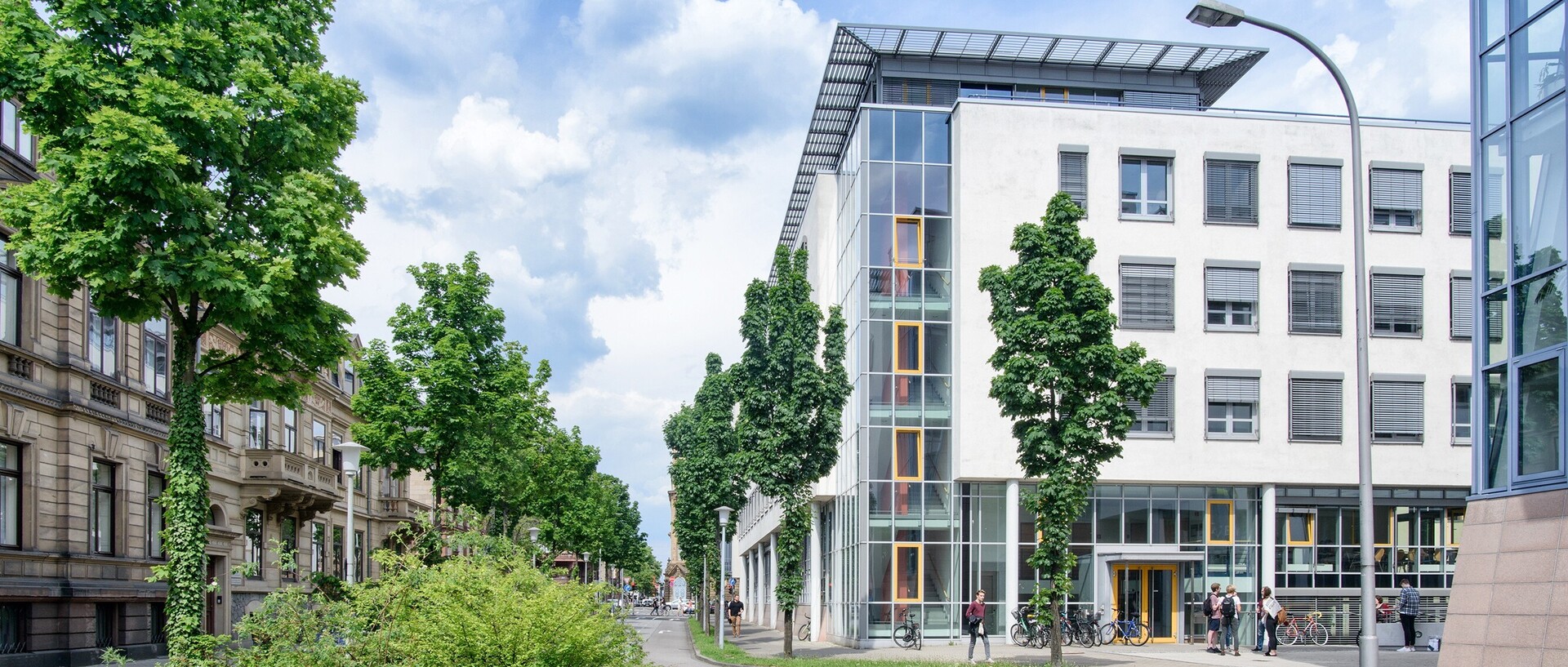 Blick auf die Rückseite des Gebäudes der Abteilung Volkswirtschaftslehre. Im Vordergrund befinden sich eine Straße und einige Bäume.