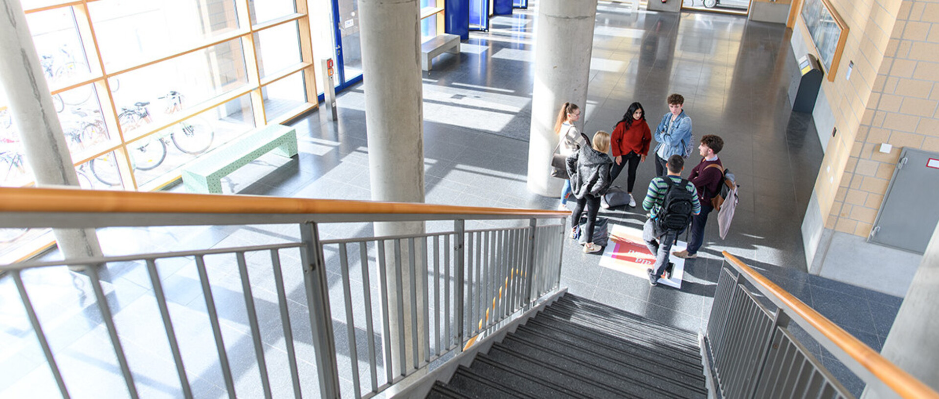 Eine Gruppe von Studierenden steht im Foyer von Gebäude B6 in einem Kreis und unterhält sich. Aufgenommen vom oberen Teil einer Treppe.